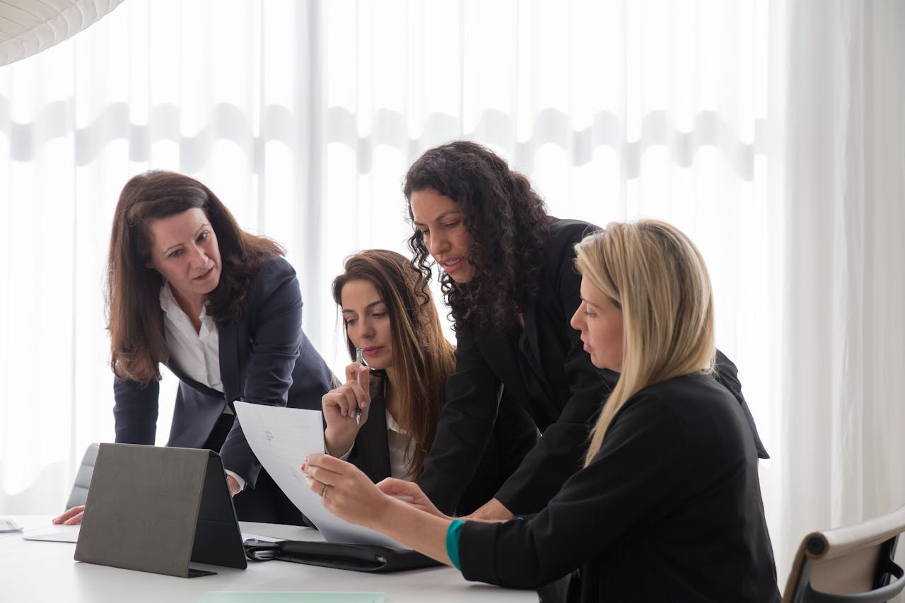 Four businesswomen engaged in discussion over documents in a contemporary office setting.